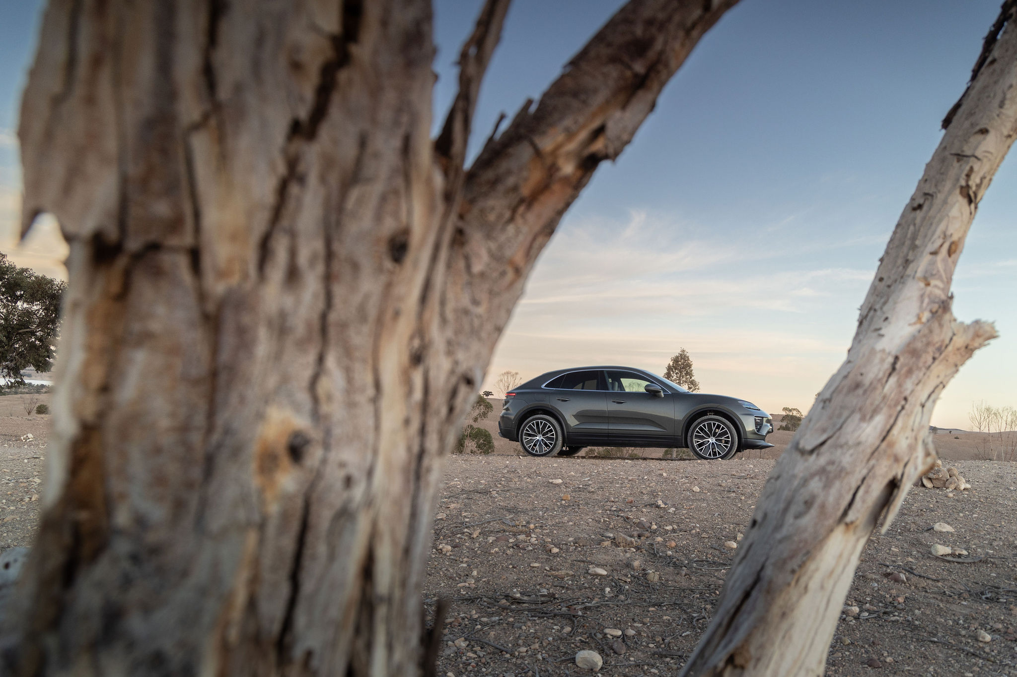 Porsche Macan électrique en arrière-plan vu à travers un arbre dans le désert d’Agafay